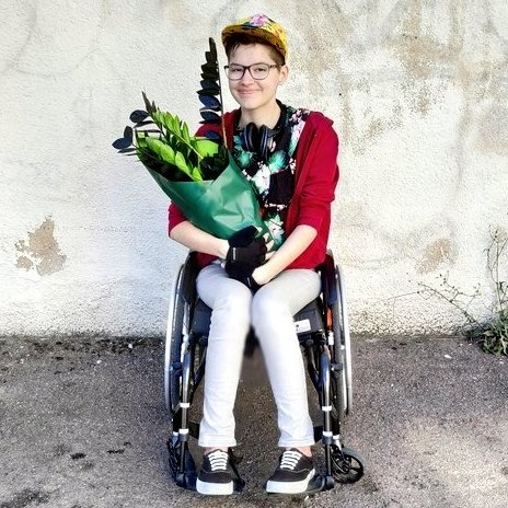 Matthieu de face, assis dans son fauteuil roulant une plante sur les genoux